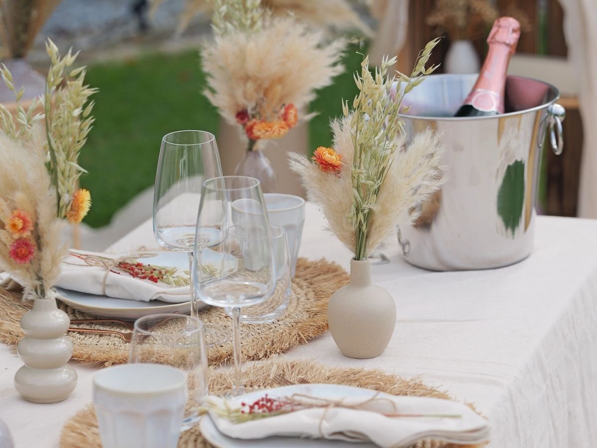 Gedeckter Picknicktisch für zwei mit Trockenblumen, Weingläsern und Sektkühler mit Rosé-Sekt